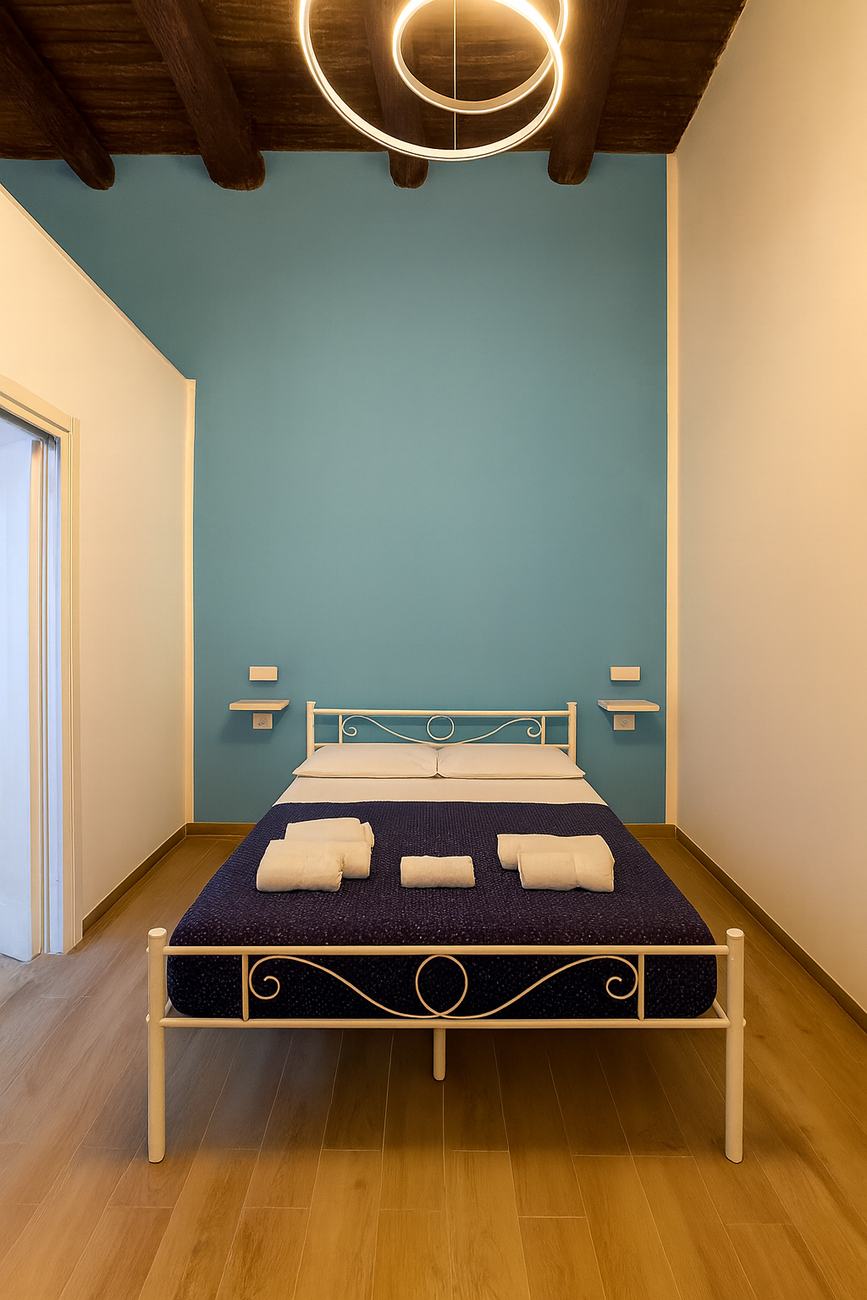 Camera con parete ottanio, letto in ferro battuto e lampada a cerchi