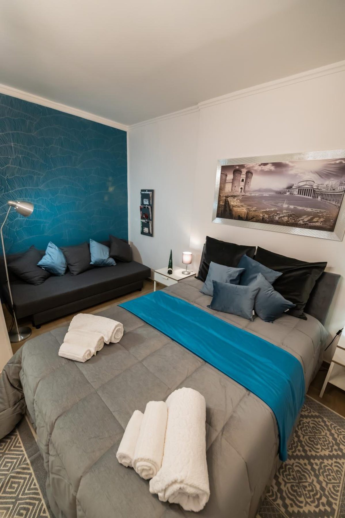 Room with a teal wall, grey bedspread and folded towels