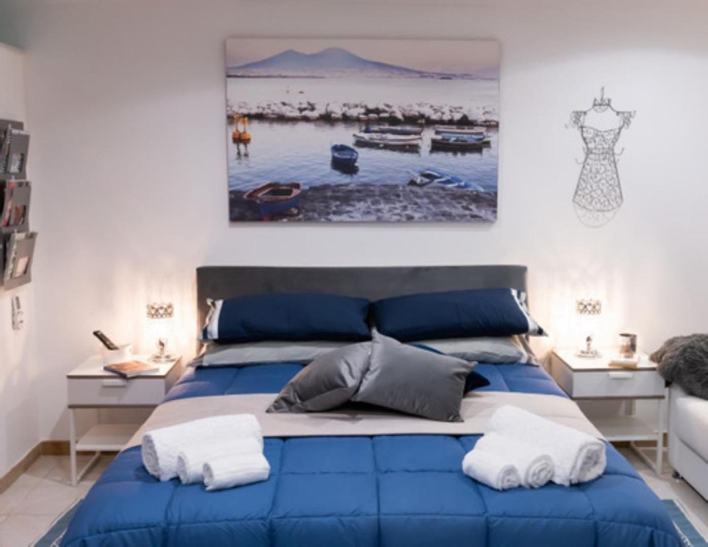 The bed beneath the canvas of Vesuvius, with two bedside lamps